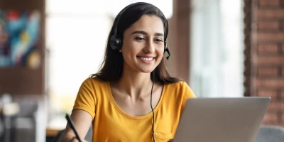 Woman with headset smiling from behind a computer screen
